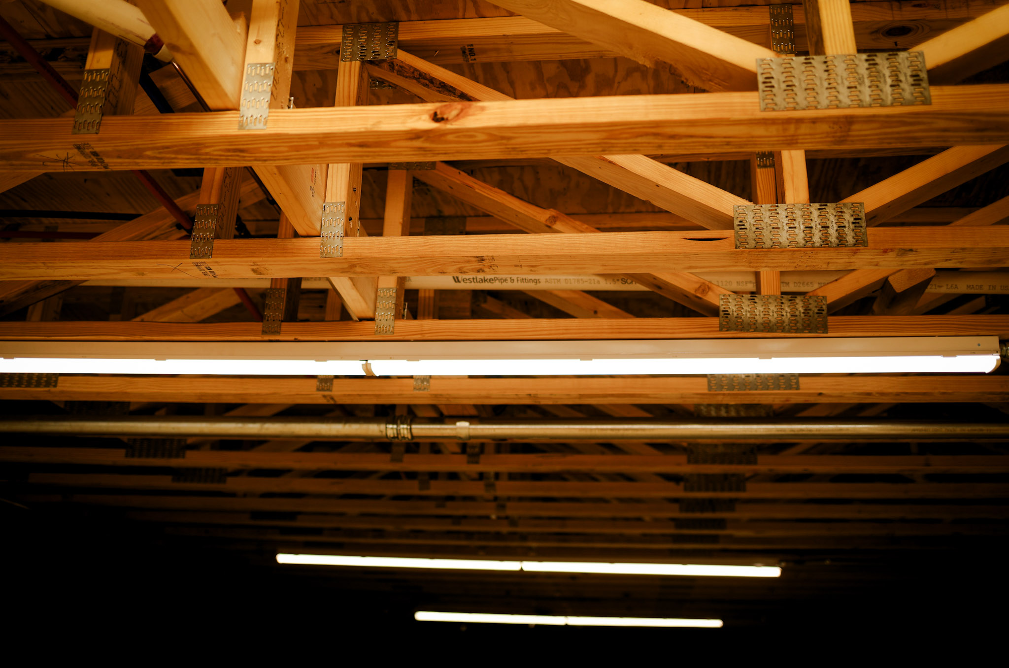Exposed wooden ceiling beams and metal brackets are visible, with several long fluorescent light fixtures hanging below them, illuminating the structure.