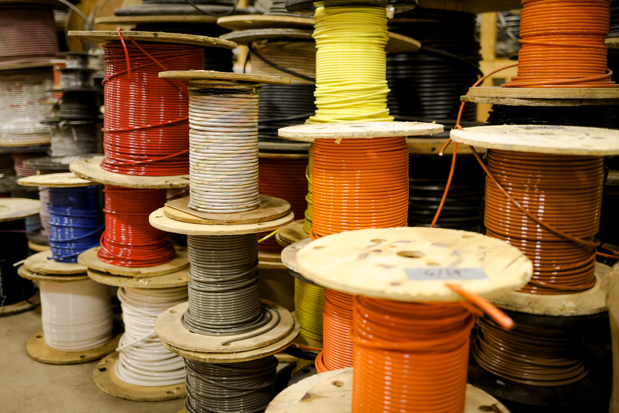 Large wooden spools filled with colorful electrical wires, including red, yellow, orange, brown, and white, are stacked in a workshop or storage area.